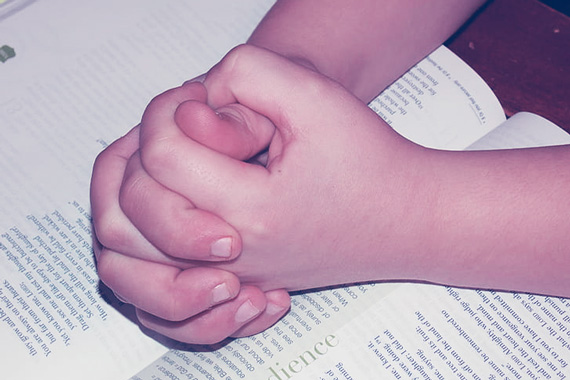 child hands praying with Bible